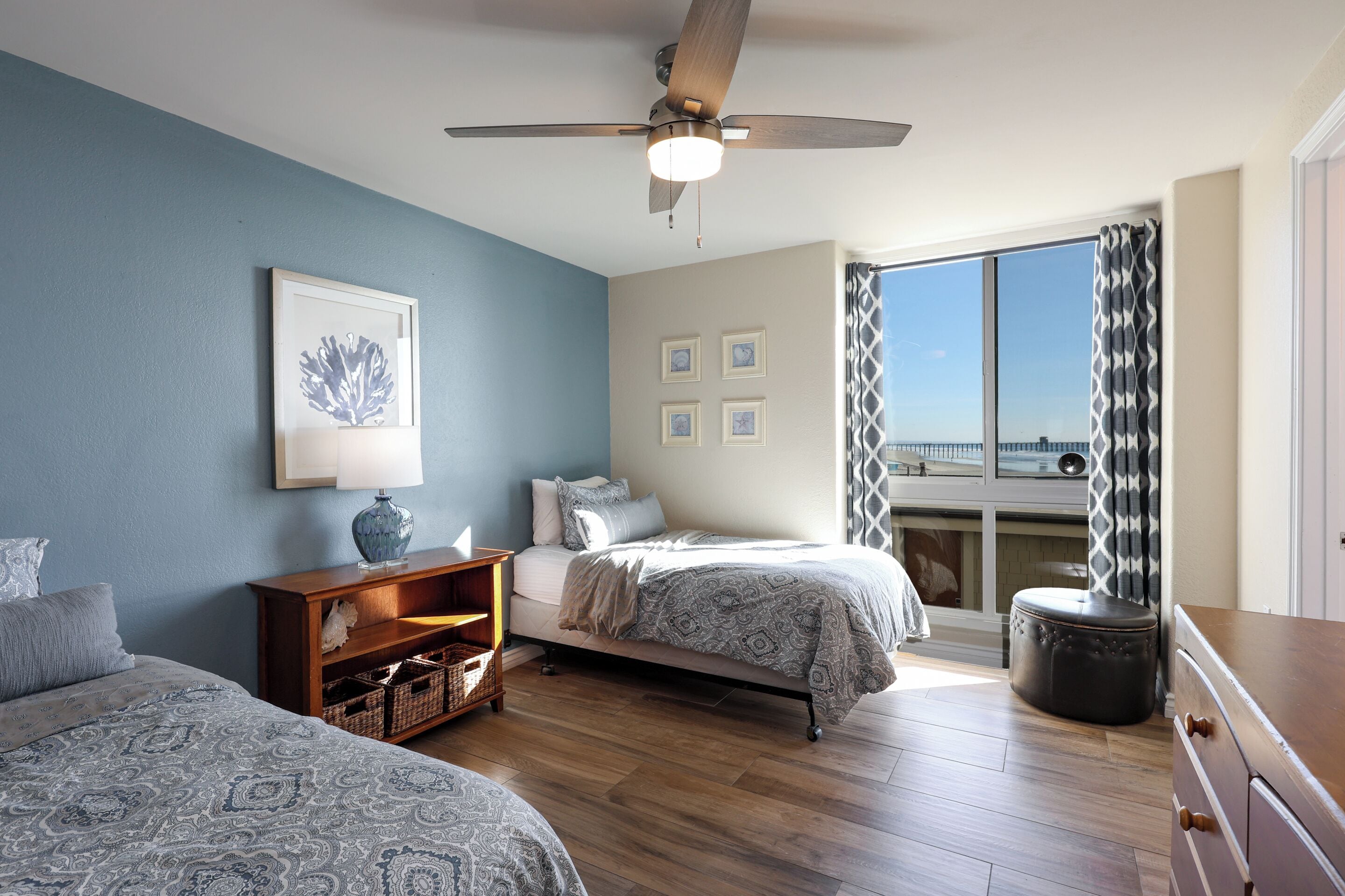 Un dormitorio con cama, mesita de noche, cómoda, ventilador de techo y ventana con vistas.