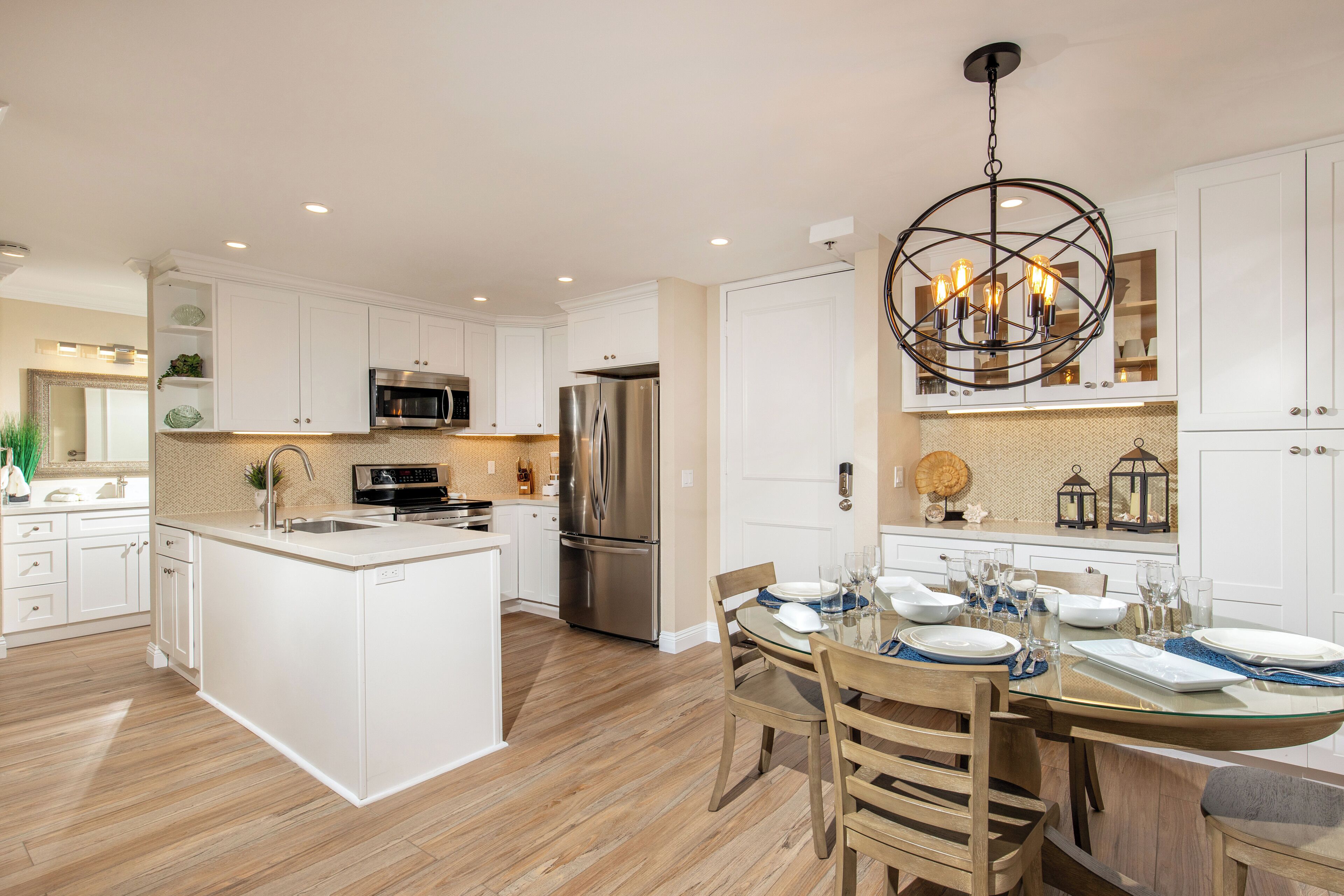 A modern kitchen with white cabinetry, stainless steel appliances, and a dining area with a glass table and wooden chairs.
