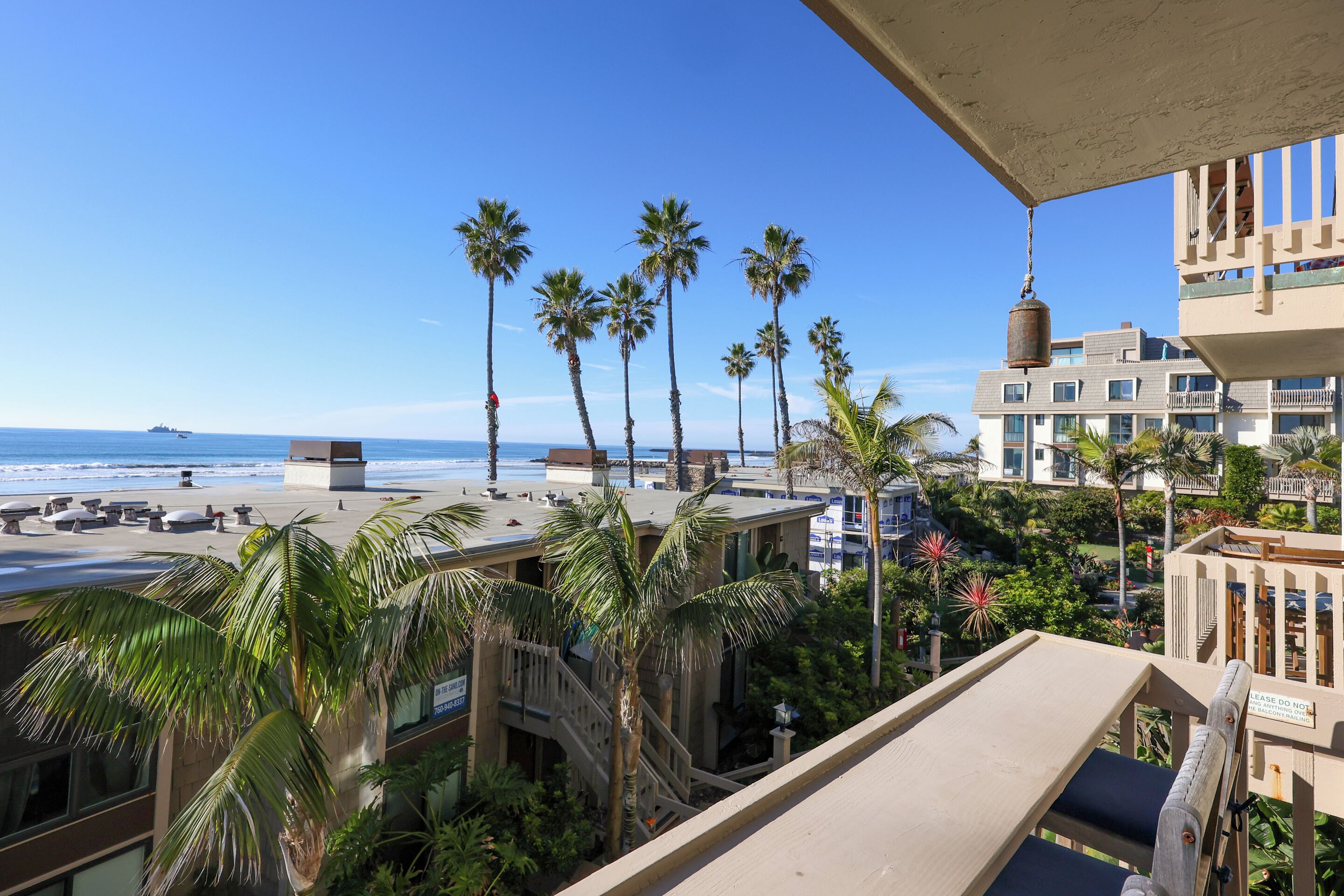 Un balcon avec vue sur la plage, les palmiers et un immeuble portant une enseigne.