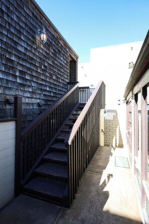 Una escalera exterior estrecha con barandilla de madera que lleva a la entrada de un edificio.