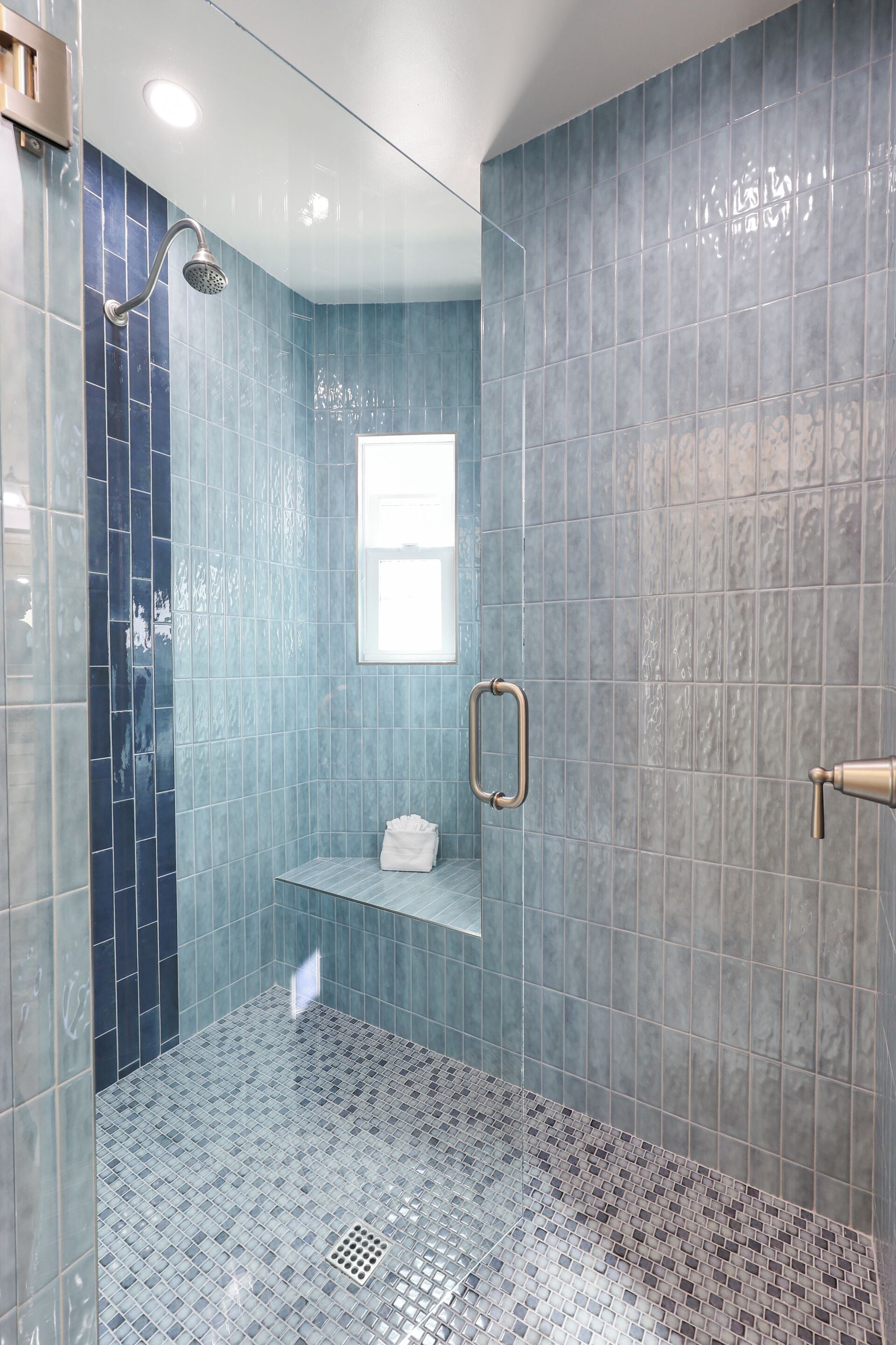Un bagno moderno con piastrelle blu, una doccia, un piccolo oblò e un porta asciugamani.