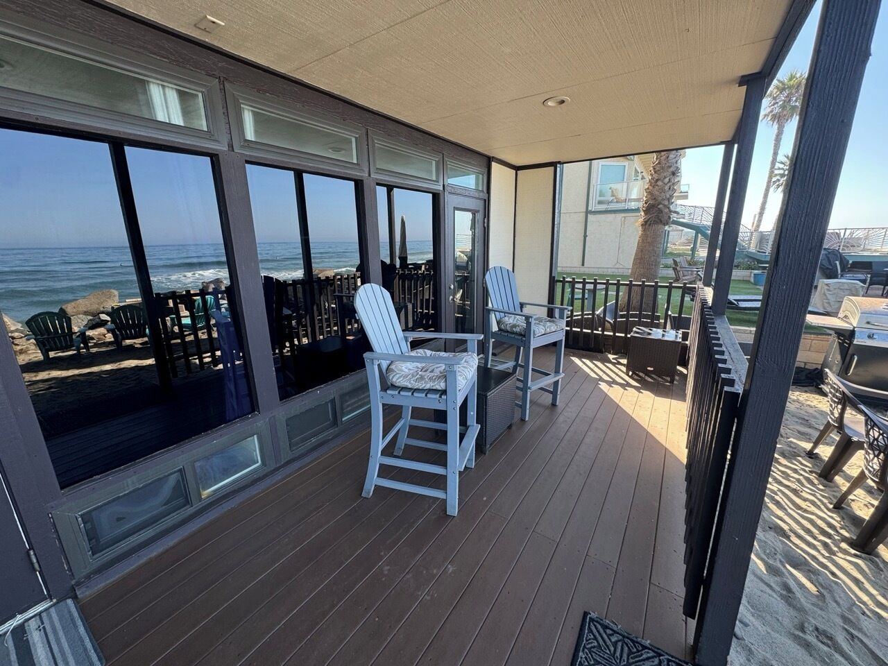 Ein überdachter Außenbereich mit Holzterrasse, zwei weißen Stühlen und Blick auf das Meer.