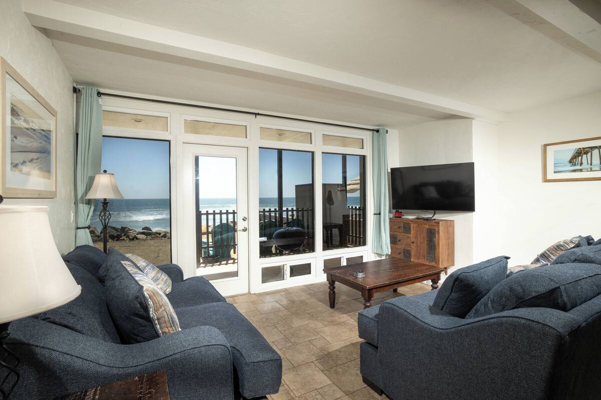 A living room with a view of the ocean, a television, and a wooden cabinet.