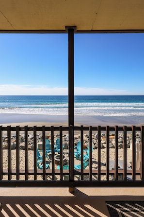 A beach view from a covered area with a wooden fence, blue chairs, and a table. - Beachfront Retreat (Oceanside)