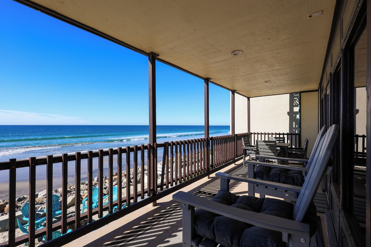 A covered outdoor seating area with a view of the beach and ocean.