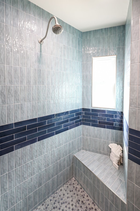 A bathroom with blue and white tiles, a showerhead, and a bench. - Beachfront Retreat (Oceanside)