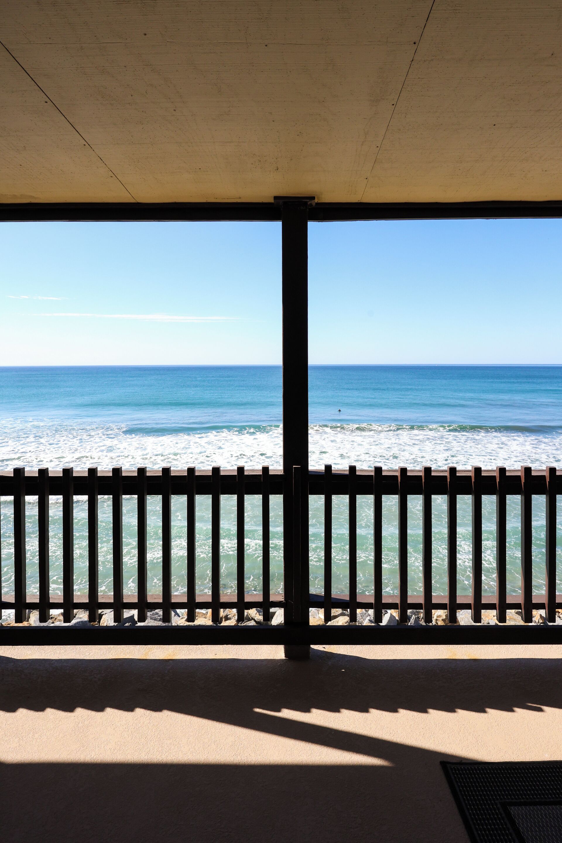 A beach view from a covered area with a wooden fence.