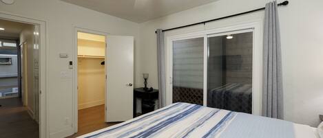 A bedroom with a bed, a ceiling fan, a sliding glass door, and a small table with a lamp.