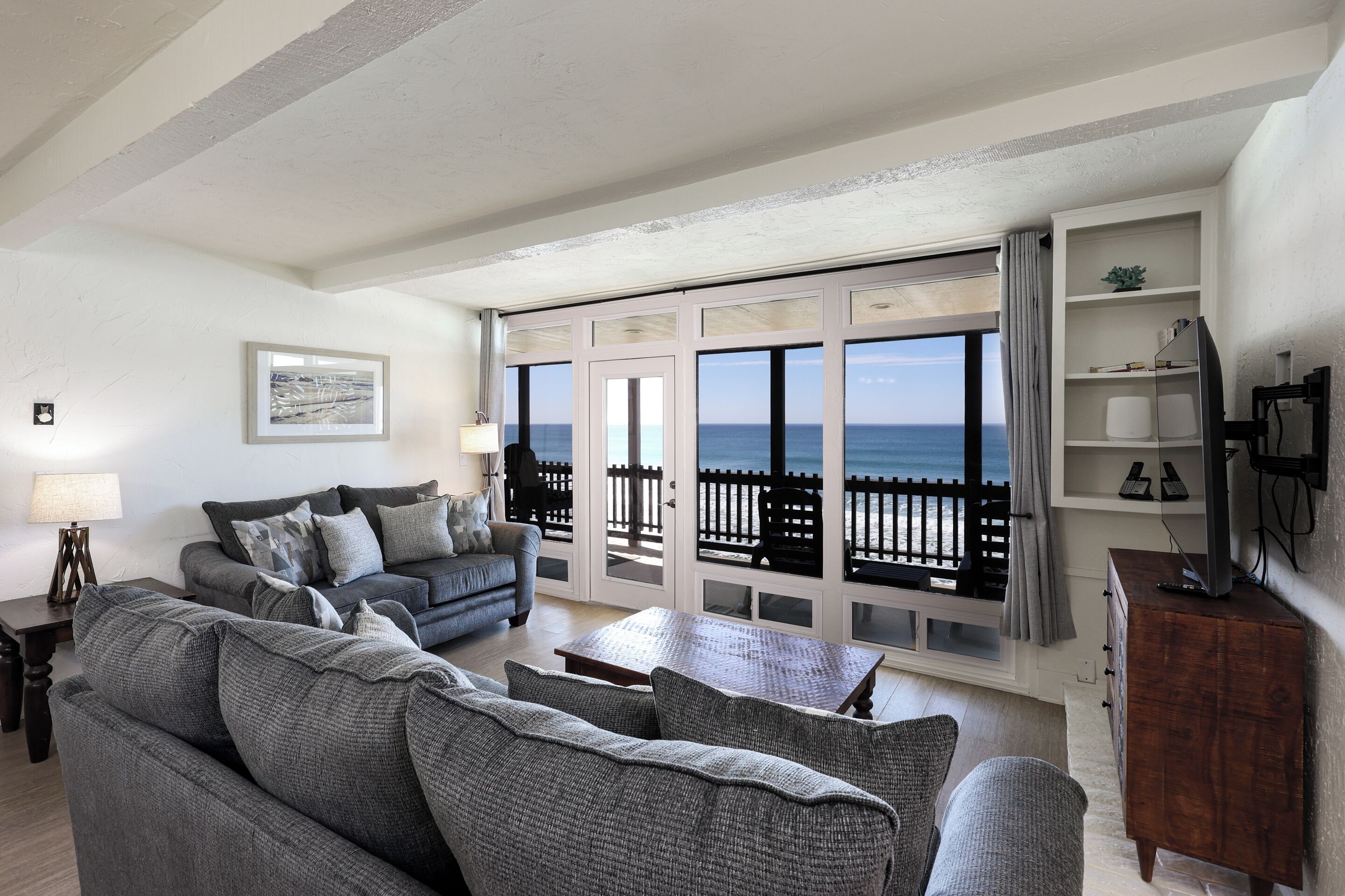 Un soggiorno con un'ampia finestra vista mare, un divano, un tavolino da caffè e una TV su un mobile in legno.