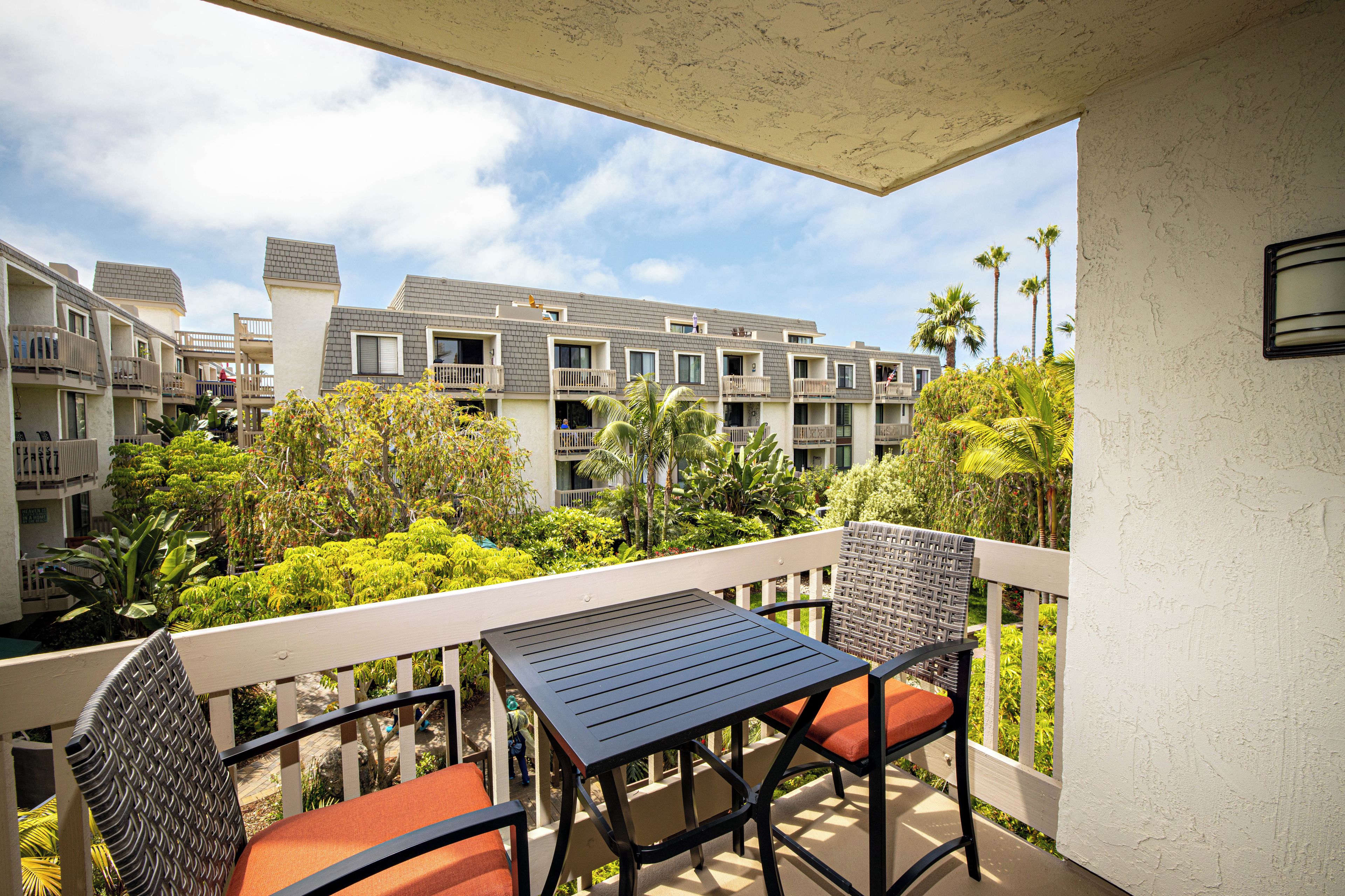 A balcony with a table and chairs, overlooking a residential area with multiple buildings and lush greenery.