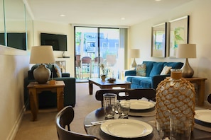 A living room with a sofa, a dining table set for two, and a TV mounted on the wall. - Oceanside Beach Condos (Oceanside)