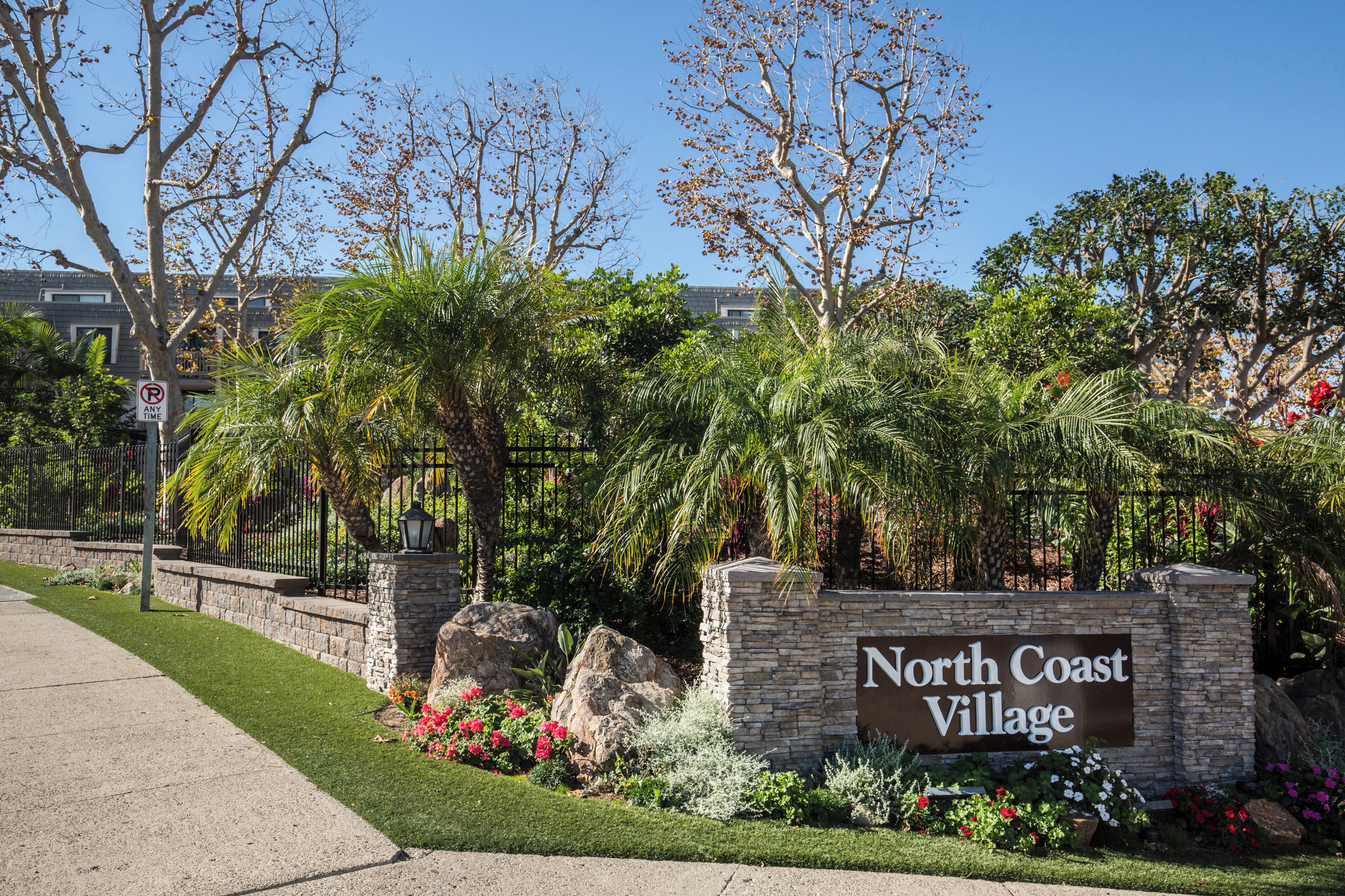 A sign for North Coast Village with a stone wall and landscaped garden.