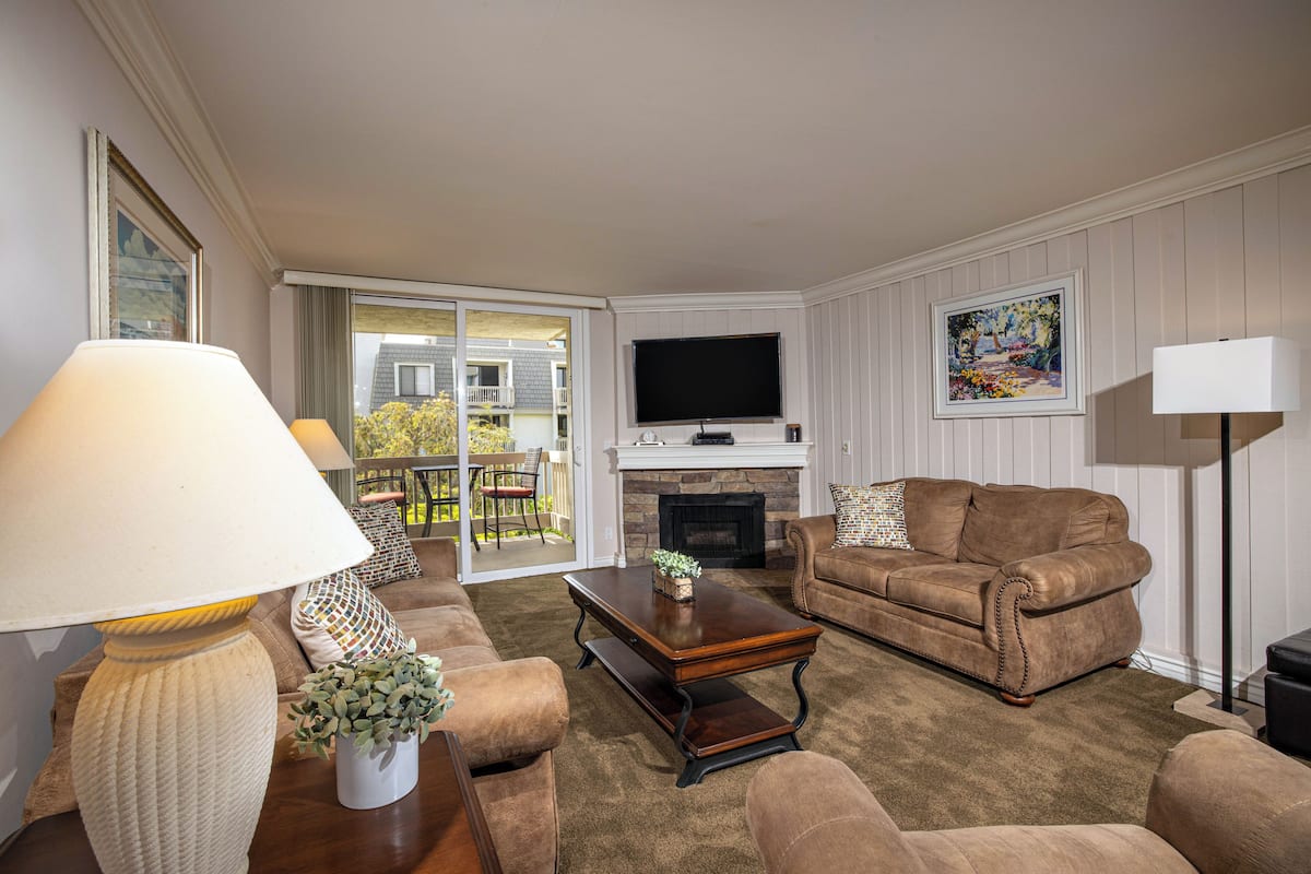 A living room with a sofa, armchair, coffee table, and a flat-screen TV mounted above a fireplace.