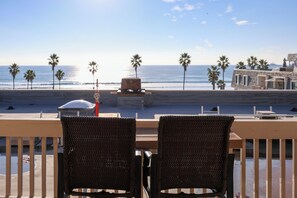A balcony with wicker chairs overlooking a beach with palm trees and a stone building in the background. - Oceanside Beach Condos (Oceanside)