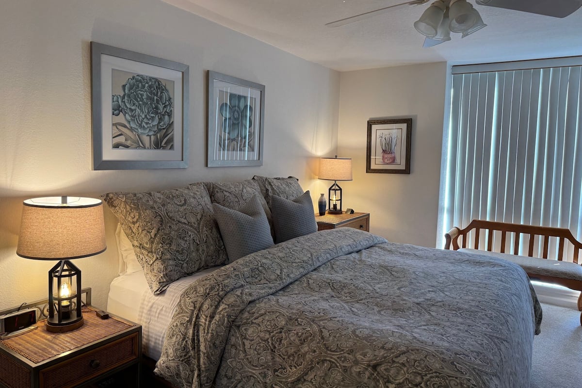 A bedroom with a bed, nightstands, a lamp, and framed artwork on the wall.