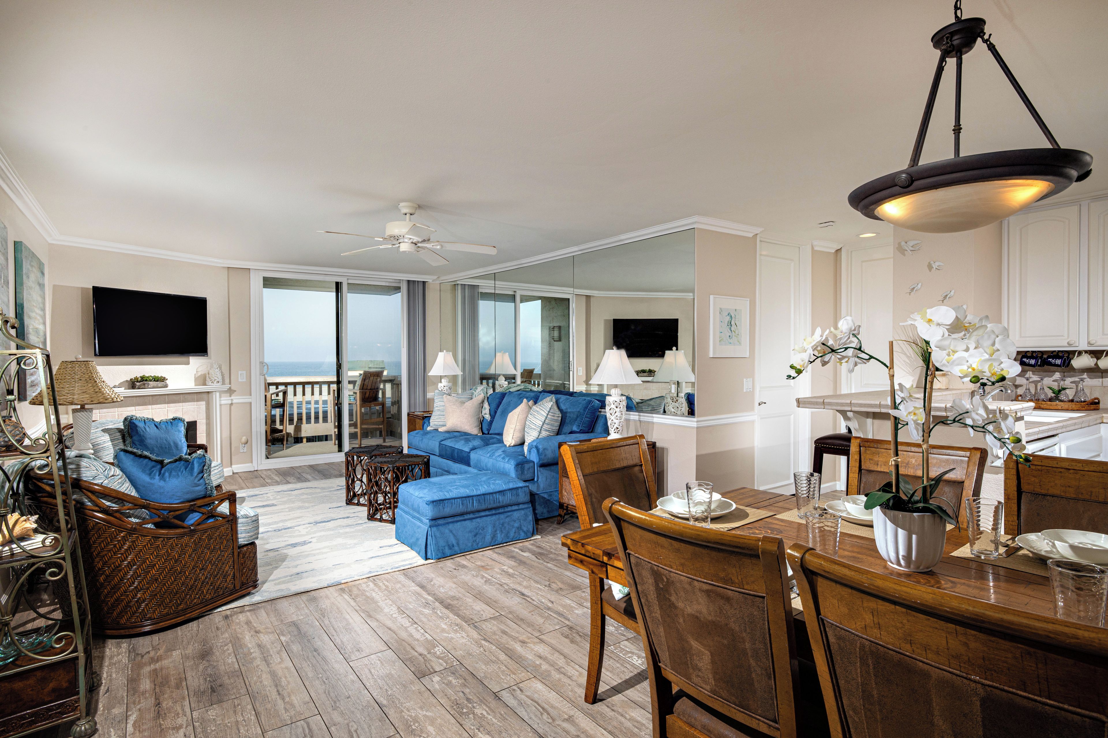 A spacious living room with a blue sofa, wooden dining table, and a balcony with a view.