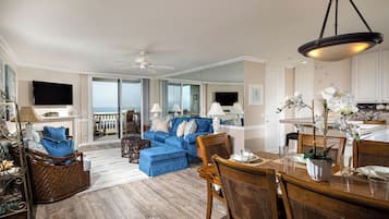 A spacious living room with a blue sofa, wooden dining table, and a balcony with a view.