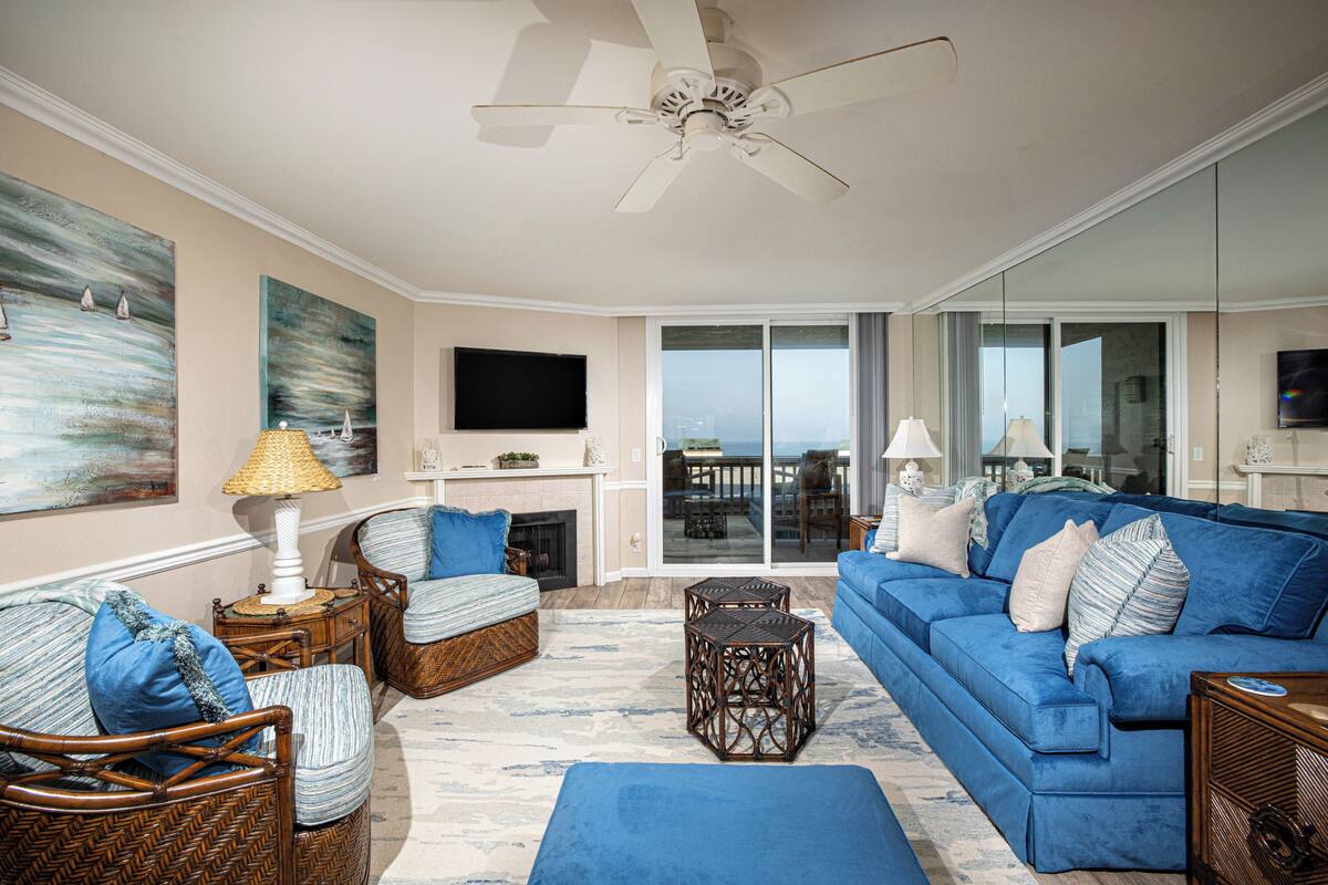A living room with a blue sofa, wicker chairs, a fireplace, and a large window offering a view.