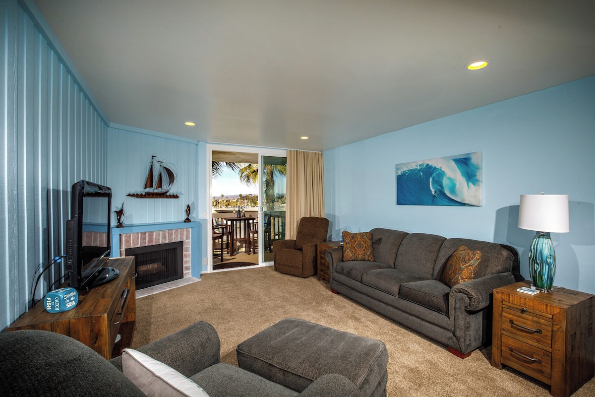 A living room with a fireplace, a sofa, a television, and a view of the outdoors.