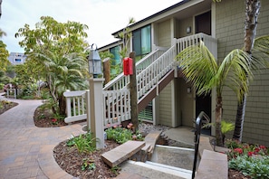 A residential building with a white staircase, a front porch, and a garden with various plants and flowers. - Oceanside Beach Condos (Oceanside)