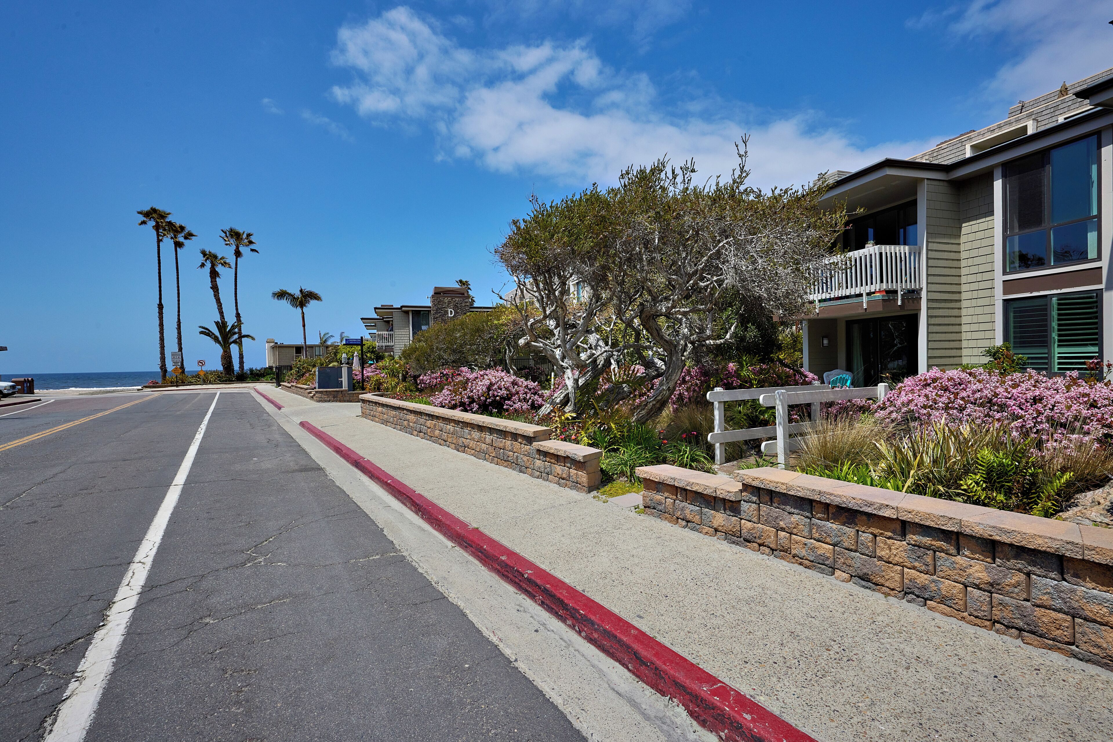 A coastal street with modern houses, a sidewalk, and a clear blue sky.