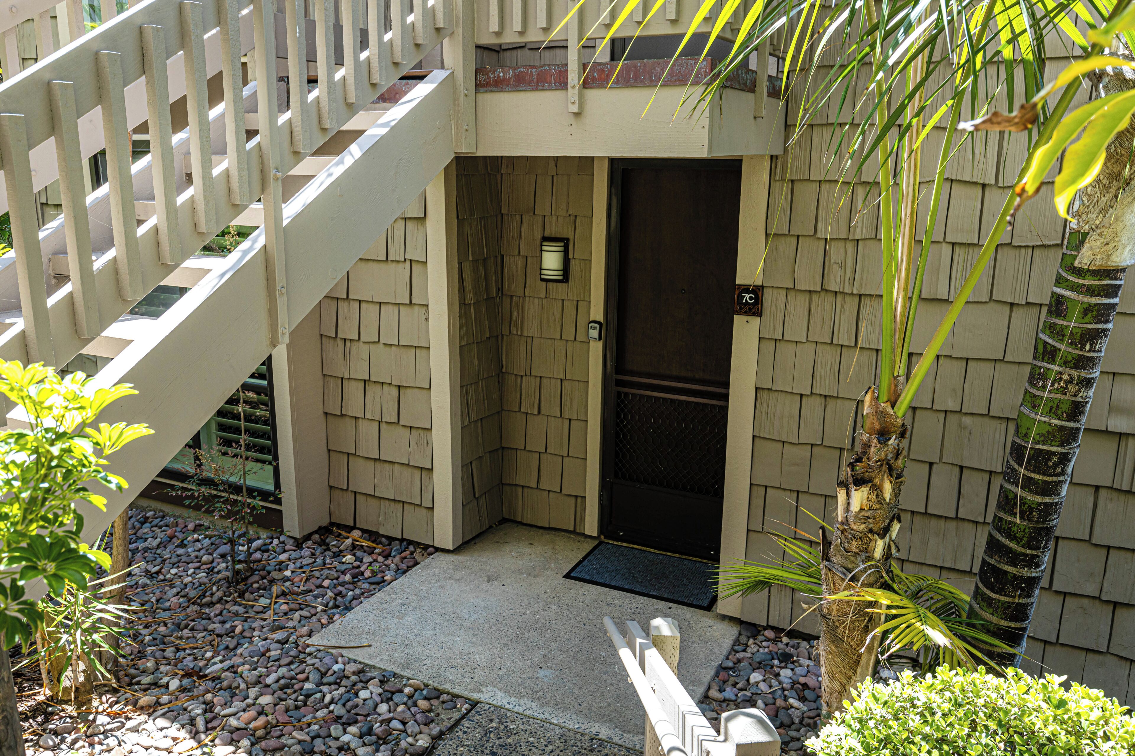 A building entrance with a wooden door, a metal gate, and a small garden area with rocks and plants.