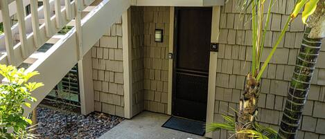 A building entrance with a wooden door, a metal gate, and a small garden area with rocks and plants.