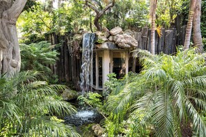A waterfall cascading over rocks into a small pond surrounded by lush greenery and a wooden structure. - Oceanside Beach Condos (Oceanside)