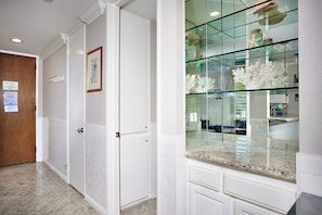 Un pasillo con paredes de azulejos blancos, una puerta de madera y una vitrina de vidrio con objetos decorativos.