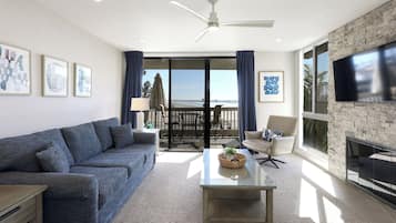 A modern living room with a blue sofa, a glass coffee table, and a TV on the wall.