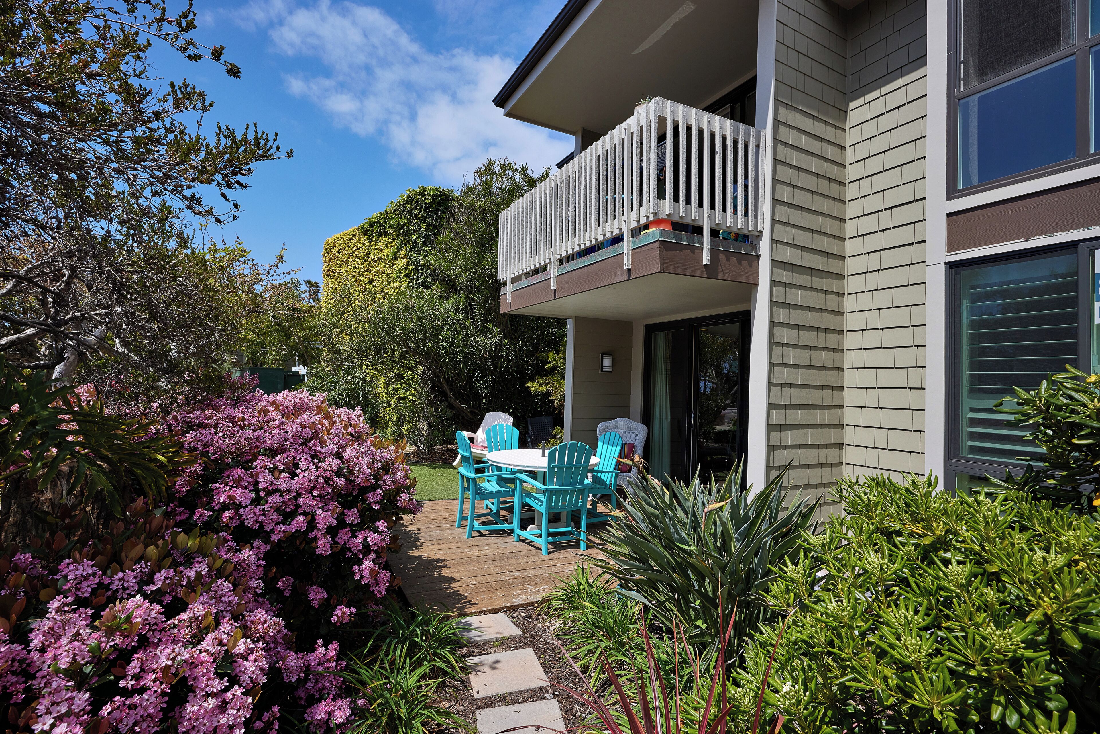 A modern house with a balcony, a wooden deck, and a garden with various plants and flowers.