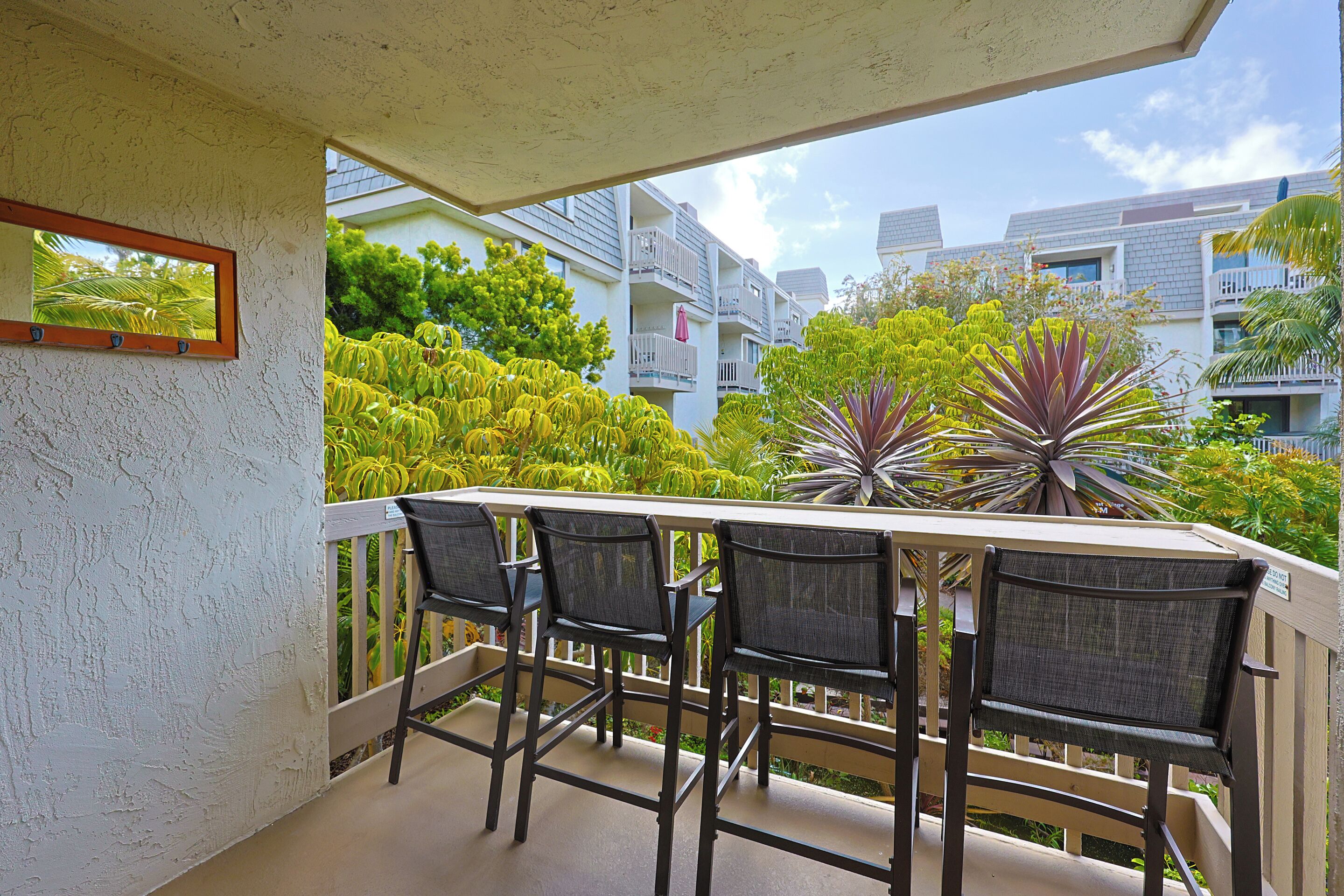 A balcony with a table and four chairs, overlooking a garden and residential buildings.