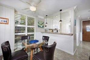 Una cocina moderna con armarios blancos, una mesa de comedor de vidrio y un ventilador de techo.