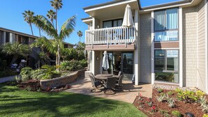 A two-story building with a balcony, outdoor patio with a table and chairs, and a garden with palm trees and plants. - Oceanside Beach Condos (Oceanside)