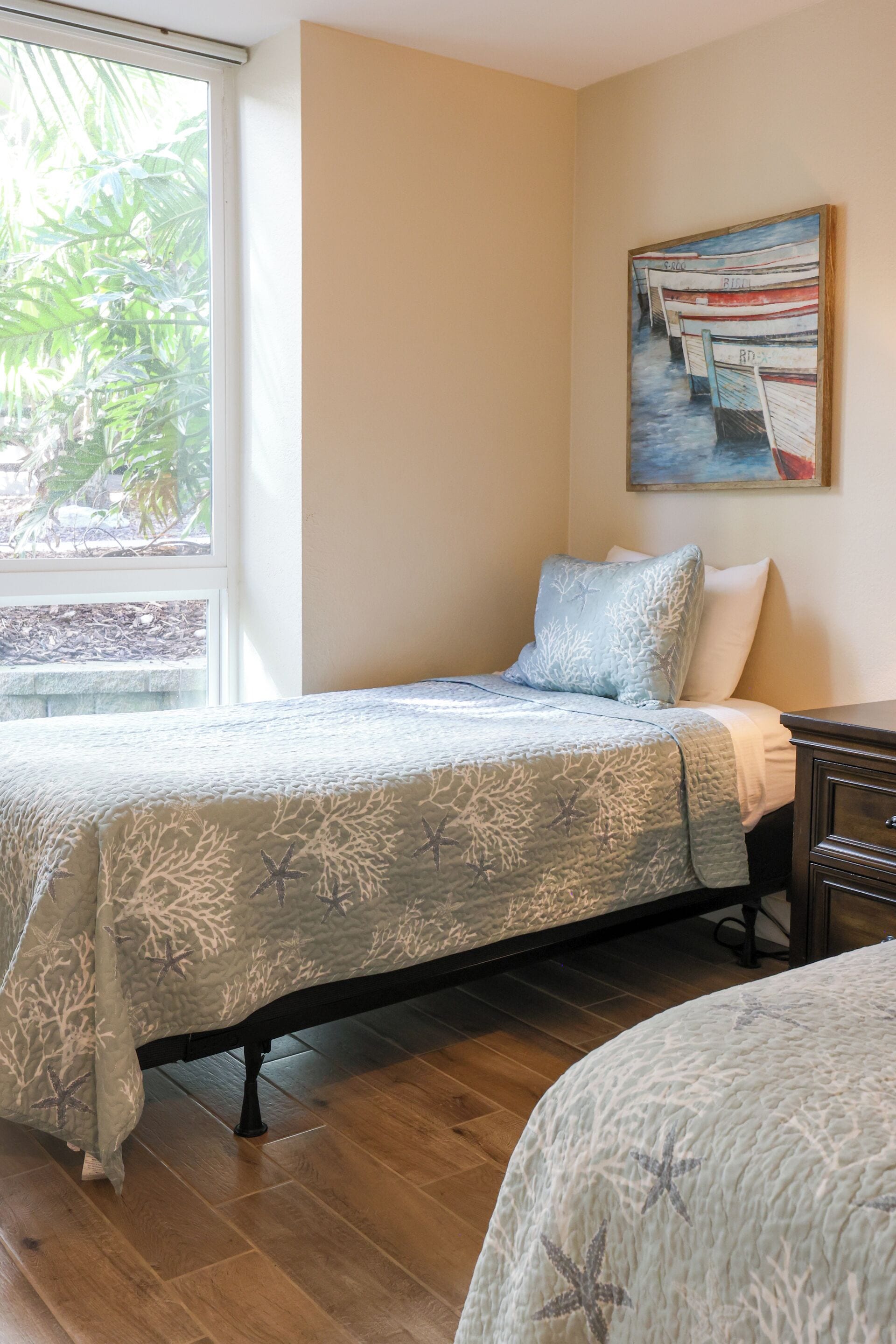 Une chambre à coucher avec un lit, une table de chevet, un tableau et une fenêtre donnant sur un paysage verdoyant.