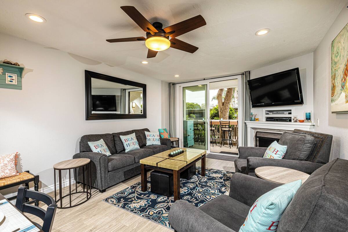 A modern living room with a ceiling fan, a flat-screen TV mounted above a fireplace, and a dining area with a table and chairs.