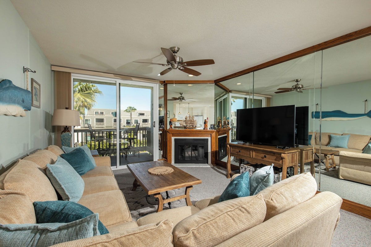 A spacious living room with a large sofa, a wooden coffee table, a flat-screen TV, and a fireplace.
