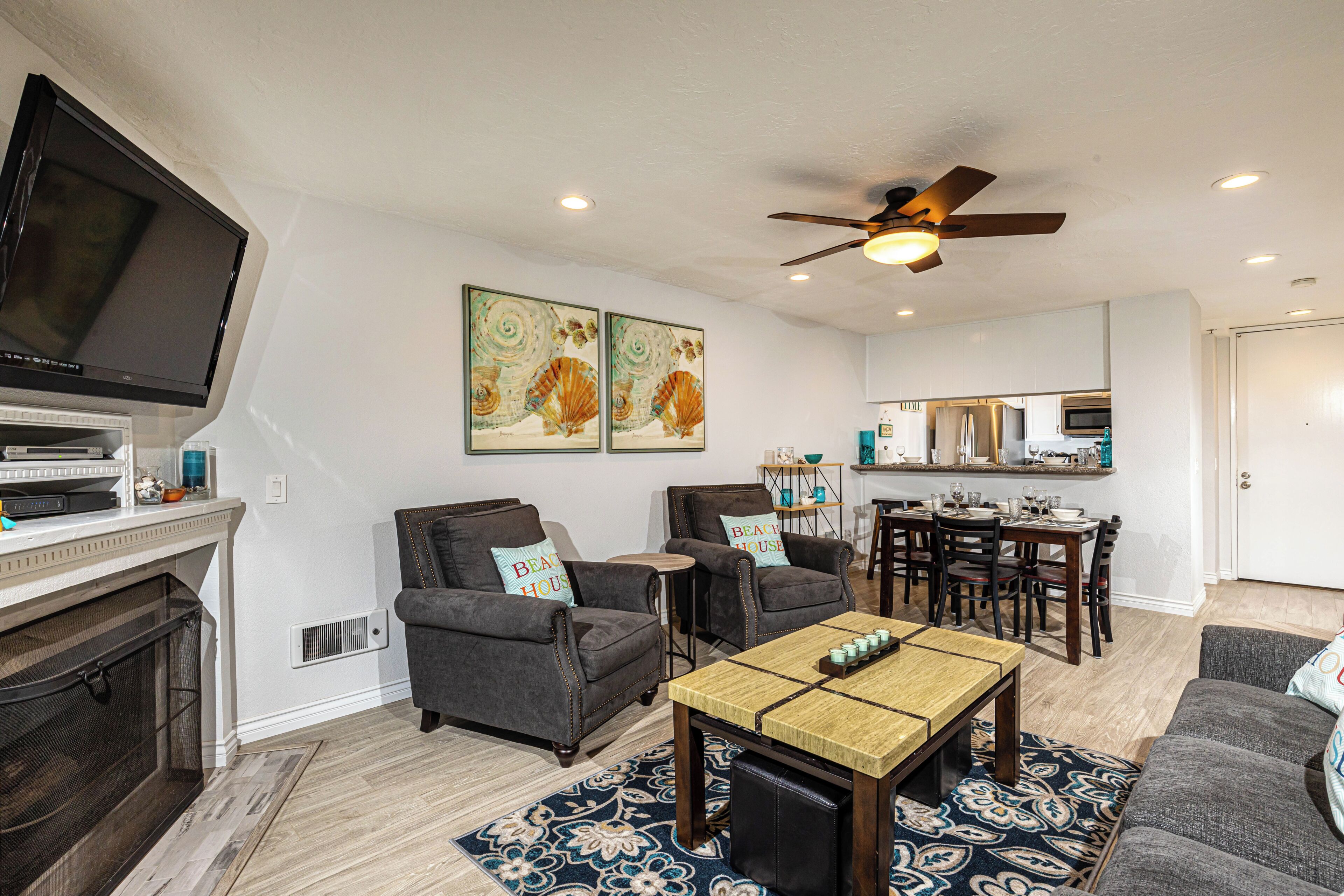 A living room with a TV, fireplace, two armchairs, a coffee table, and a dining area with a table and chairs.