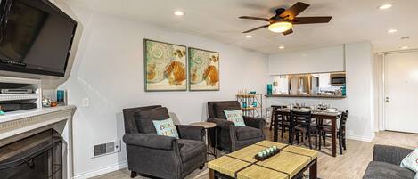 A living room with a TV, fireplace, two armchairs, a coffee table, and a dining area with a table and chairs.