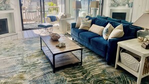 A living room with a blue sofa, white armchairs, a coffee table, and a fireplace. - Oceanside Beach Condos (Oceanside)