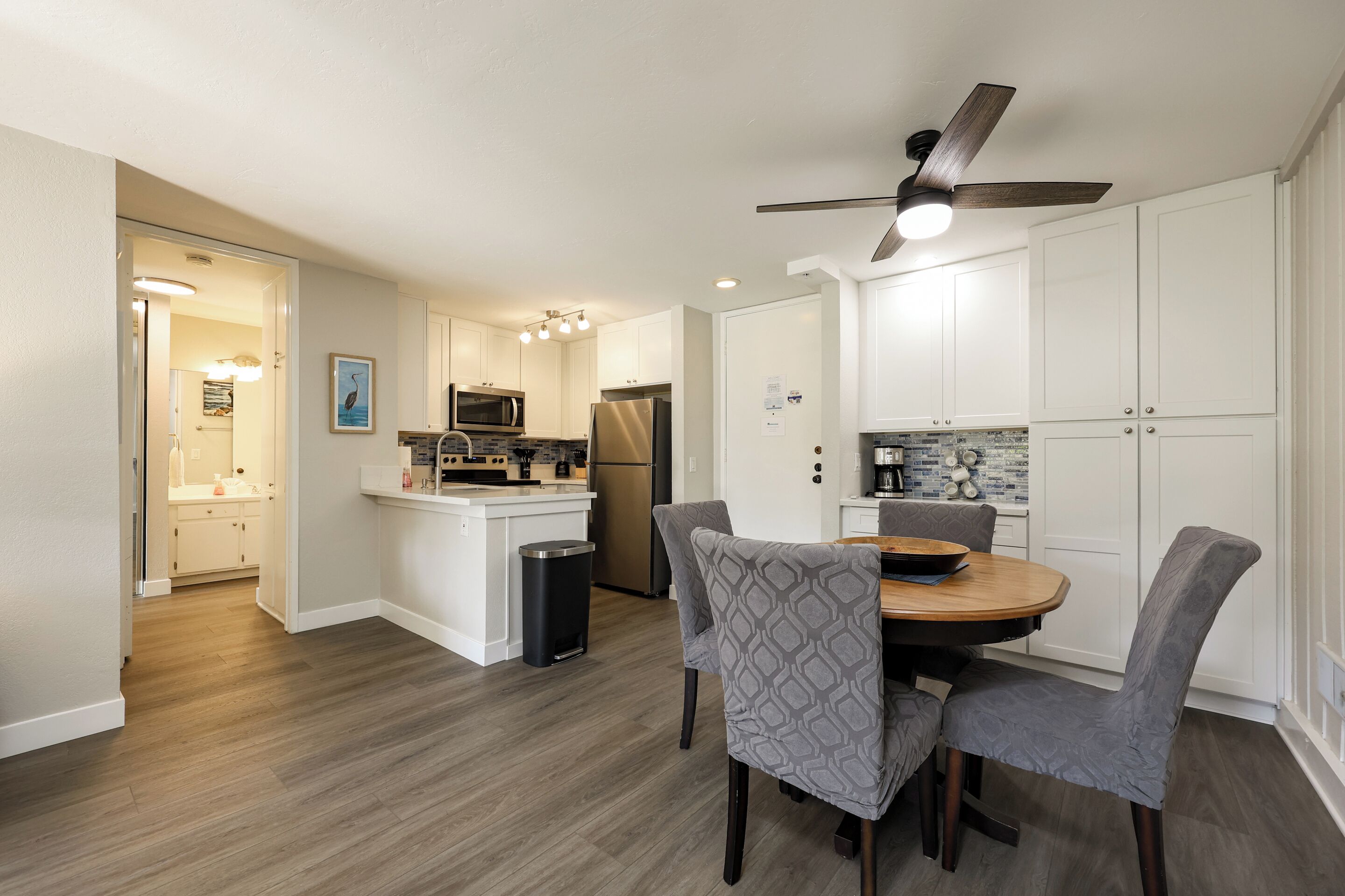 A modern kitchen with white cabinets, a microwave, and a refrigerator. There is a dining area with a table and chairs.