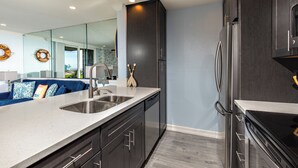 Une cuisine moderne avec des meubles de couleur sombre, des appareils en acier inoxydable et un grand îlot central doté d’un évier.
