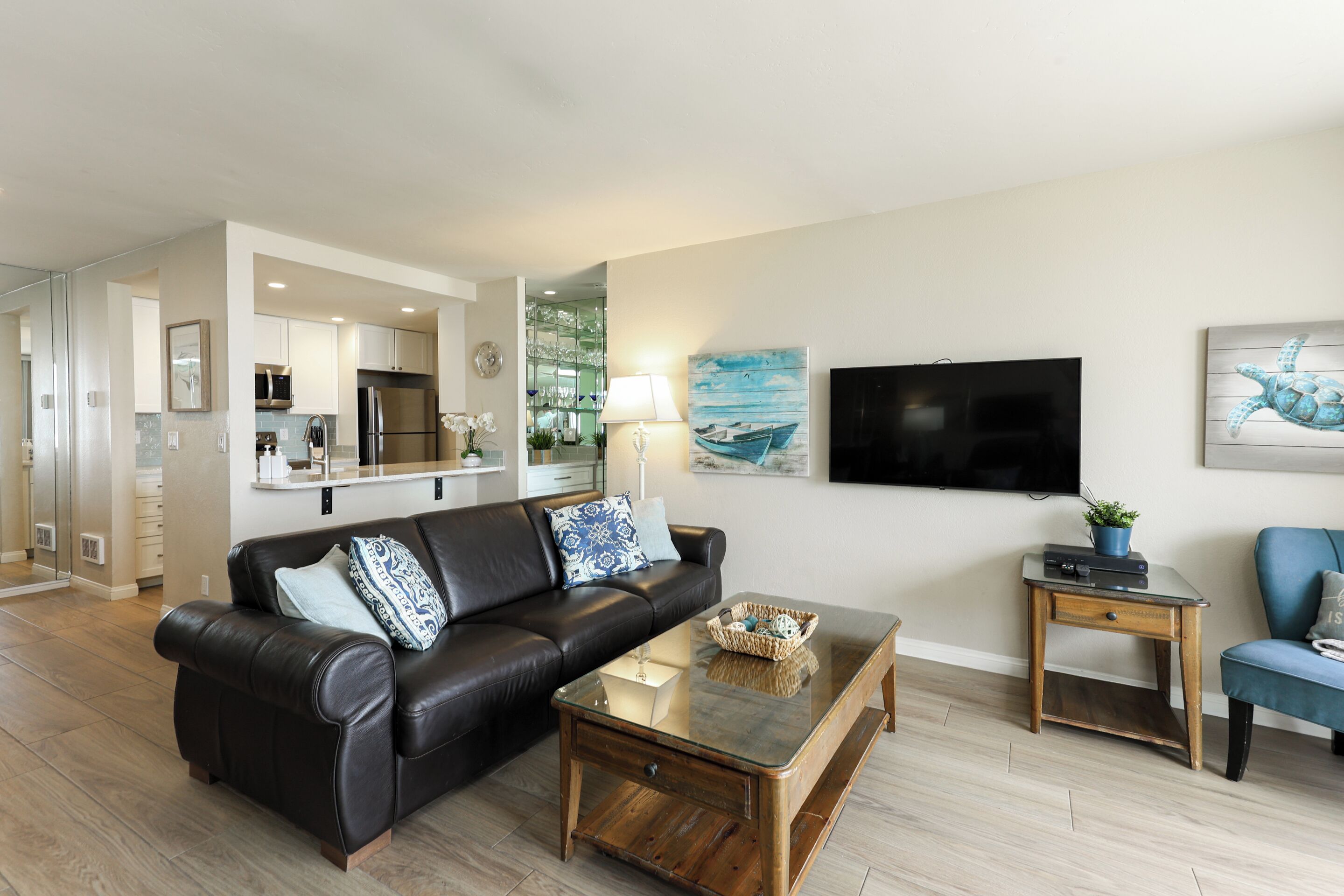 A modern living room with a leather sofa, a glass coffee table, and a flat-screen TV mounted on the wall.