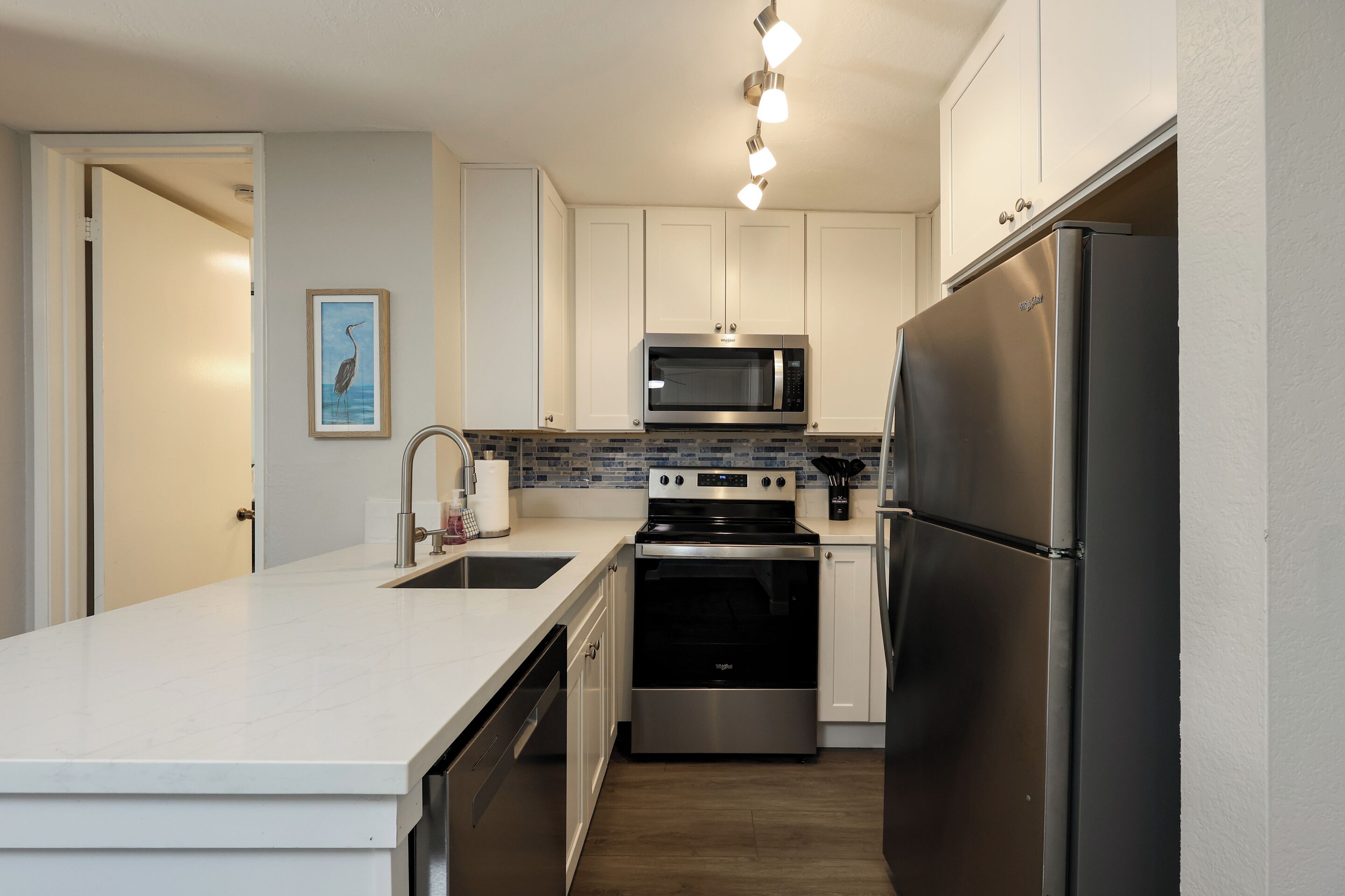 A modern kitchen with white cabinets, stainless steel appliances, and a tiled backsplash.