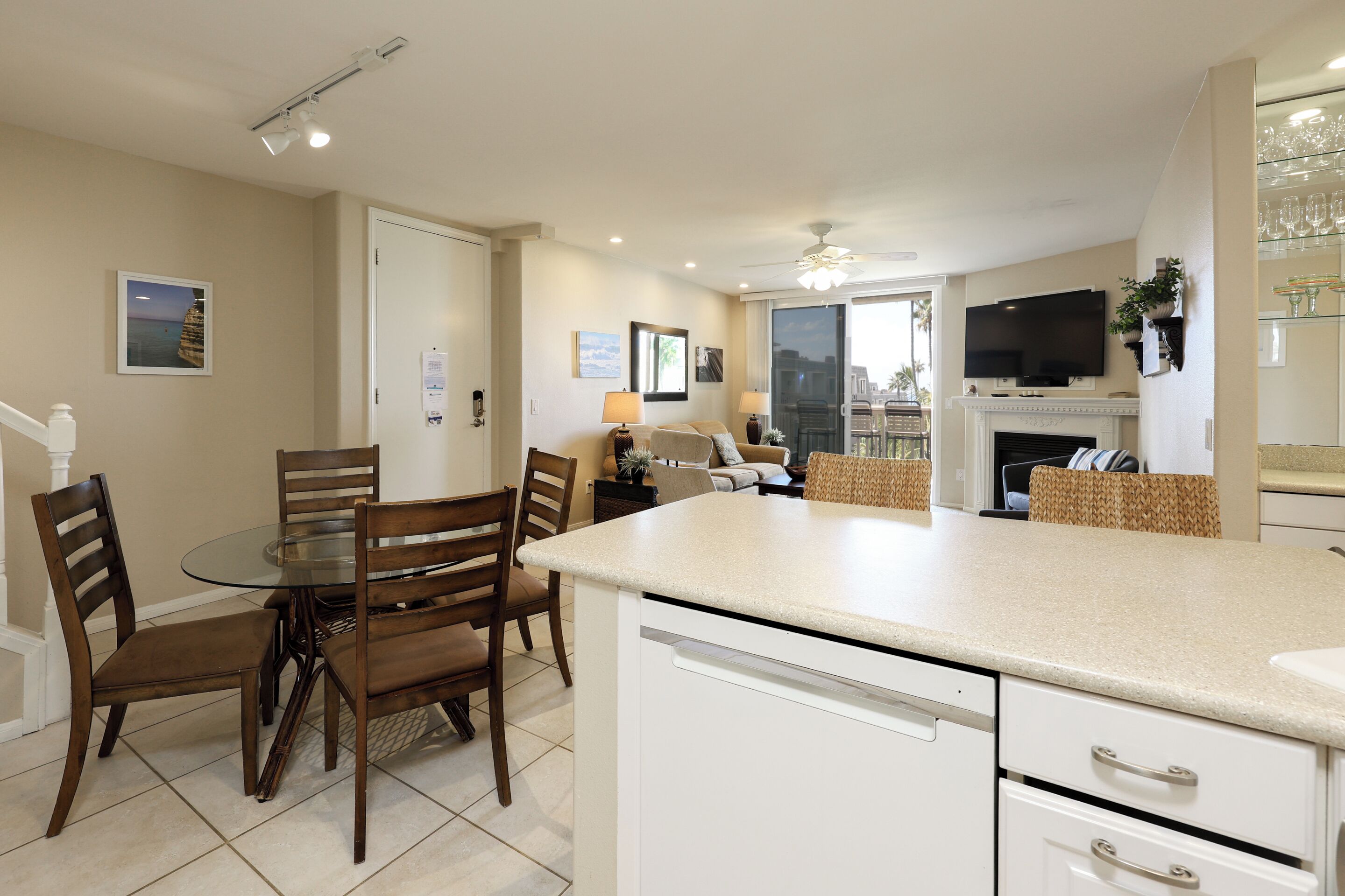 A modern kitchen with a glass dining table, white cabinetry, and a flat-screen TV mounted above the fireplace.