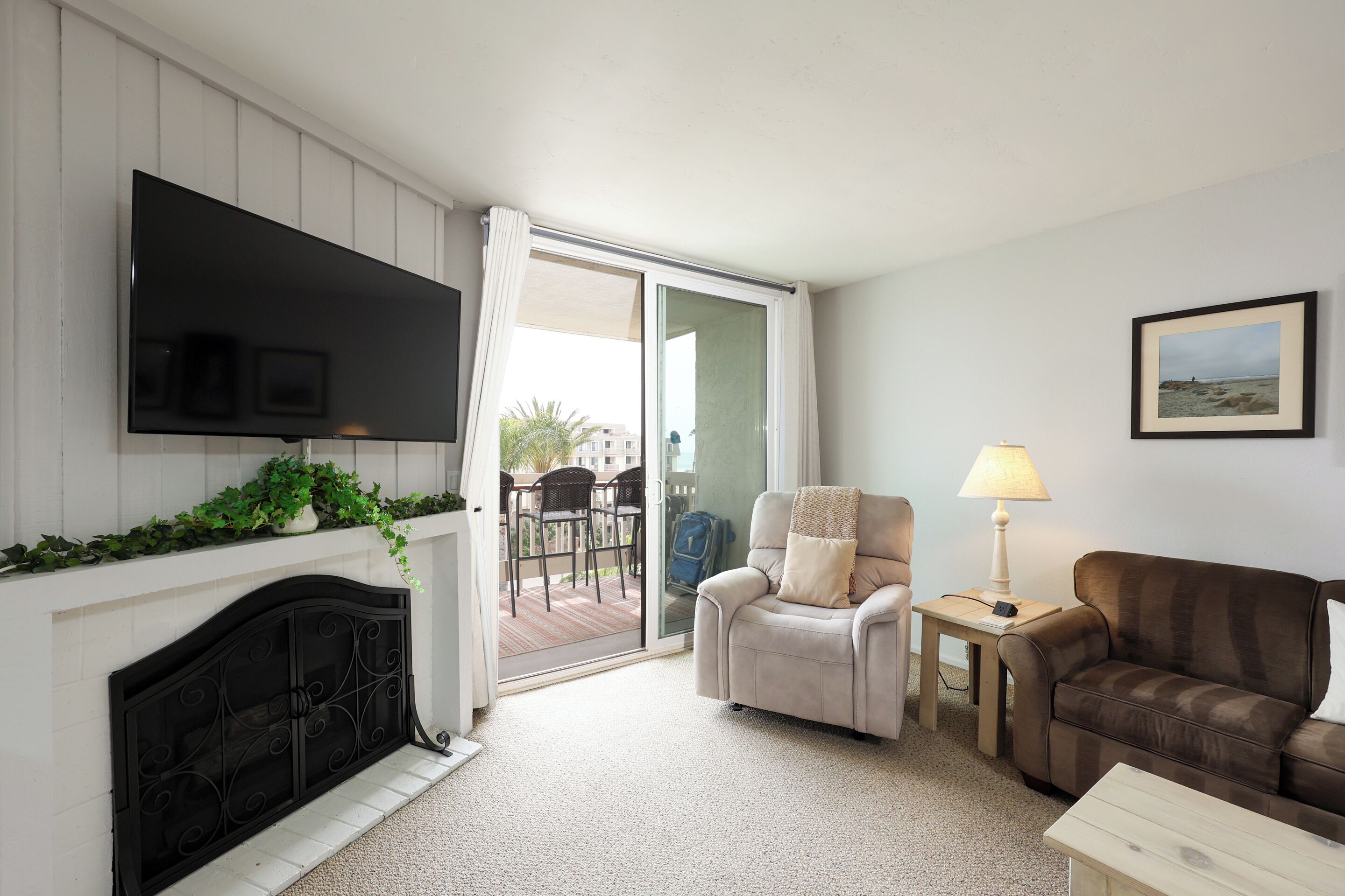 Una sala de estar con chimenea, televisor de pantalla plana, sofá, sillón, lámpara y puerta corrediza de vidrio que da a un espacio exterior.