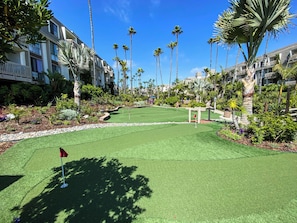 A golf course with a putting green, surrounded by palm trees and a building with balconies. - Oceanside Beach Condos (Oceanside)