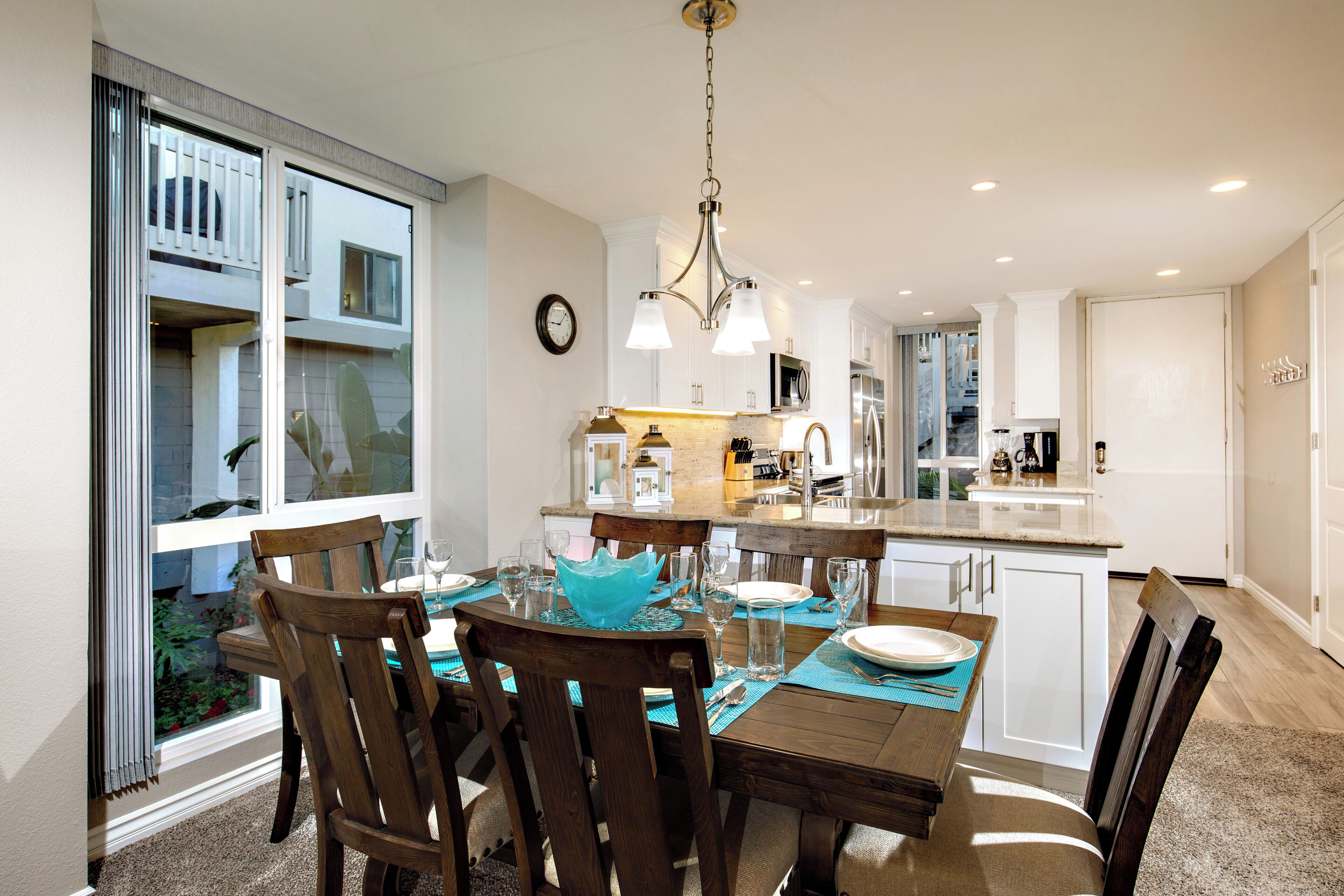 Een moderne keuken met een eethoek, voorzien van een groot schiereiland, hangende lampen en uitzicht door een schuifdeur.