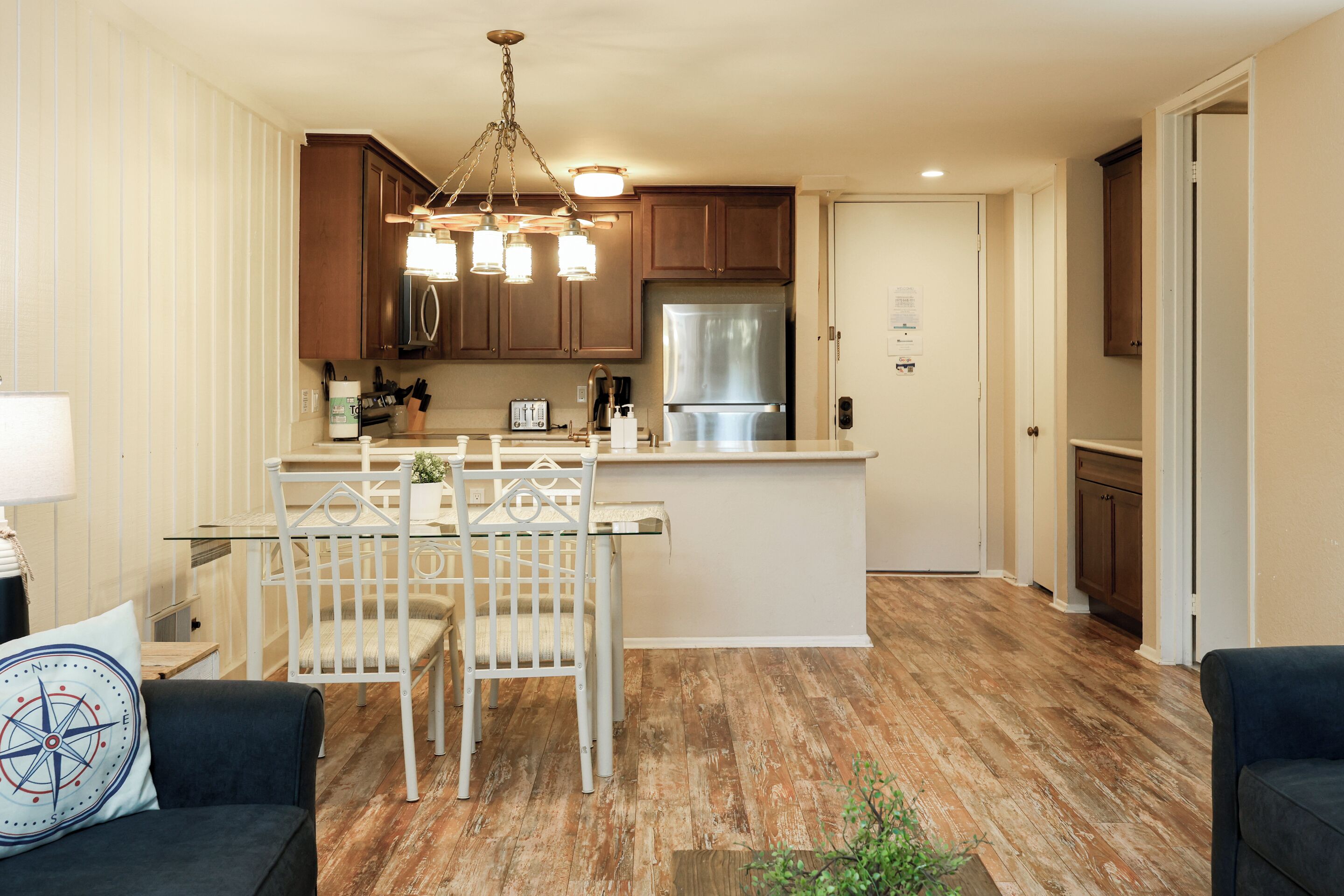 A modern kitchen with wooden cabinets, a stainless steel refrigerator, and a dining area with a glass table and white chairs.