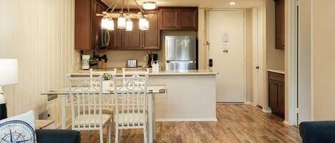 A modern kitchen with wooden cabinets, a stainless steel refrigerator, and a dining area with a glass table and white chairs.